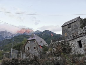Traditional village with stone houses and Albanian flags against a mountain backdrop, mountain