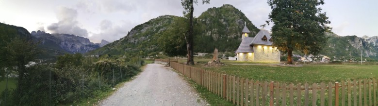 Picturesque church in Theth, a village with mountains in the background and a garden fence, Peaks
