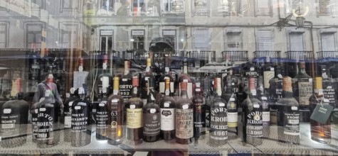 Old port wine, wine bottles and spirits in a shop window with city reflections in the background,