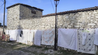 Bed sheets and towels dry on a line in front of an old stone wall, Berat, Albania