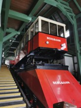 A red mountain railway is located in a covered area surrounded by green wooden structures,