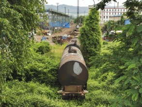 An old, rusted freight train in an industry-like setting surrounded by lush greenery, Czech