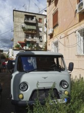 Old van, UAZ Buchanka, in front of colorful residential buildings on a sunny city street in Tirana,