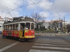 A yellow and red historic tram runs through the city under a cloudy sky, Lisbon, Portugal