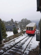 Red train goes through snow-covered mountain landscape, Oberweissbach cable car, Rennsteig,