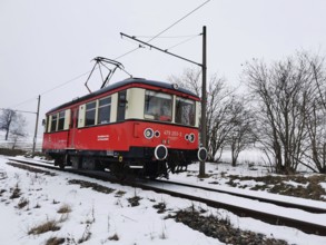 A red train moves on rails through a snowy landscape with bare trees, Bergbahn Oberweissbach,