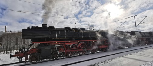 A historic steam locomotive emits smoke while standing on tracks in winter, Rennsteig, Frankenwald