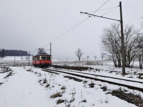 A red train travels through a snow-covered landscape, snow-covered fields in the background,