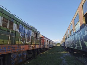 Two colorful abandoned trains full of graffiti under clear skies, Tunnelblick, Albania