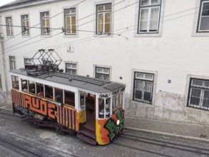 Historic funicular, Elevador da Gloria with colorful graffiti goes down a steep road, Lisbon,