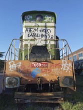 Front of a green locomotive with graffiti in daylight, Albania