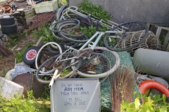 Old bikes and various objects lie messy in a garden with a warning sign, scrap collection, St
