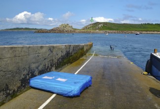 Small pier leading into the sea, colorful sky with clouds, boats and rocks in the background, St