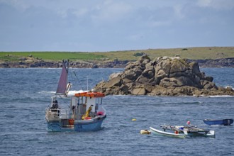 A small fishing boat out at sea off a rocky coast with colorful sails and clear skies, St Agnes,