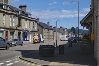 Urban street scene with cars and buildings under blue sky, Dufftown, Aberdeenshire, Scotland,