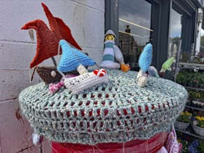 Colourful crocheted motifs of ships and houses on a wall in a maritime scene placed on a letterbox,