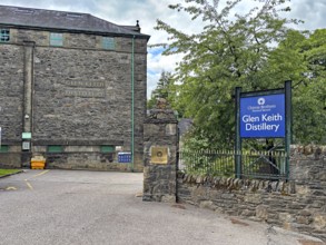 Entrance to Glen Keith Distillery with stone buildings and signs in a wooded area, Keith,