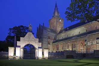 Illuminated historic church with clock tower and memorial in the evening, St Magnus Cathedral,