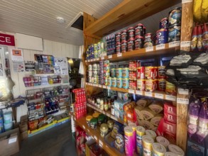 A small shop with stocked shelves full of cans and colorful food products, the only shop in the