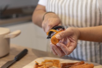 Close up of hands peeling fresh carrot in home kitchen. Healthy ingredients, simple food