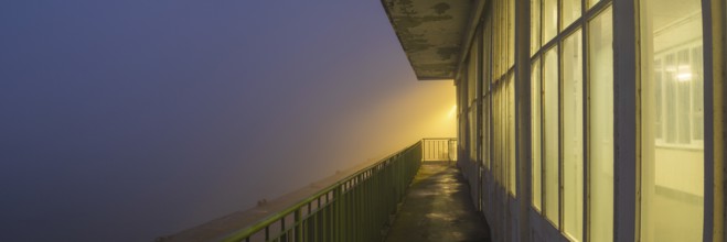 View along a long balcony of Steubenhöft at night in fog, Cuxhaven, Lower Saxony, Germany