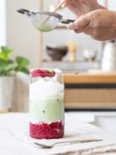Person sifting green tea powder over a refreshing iced matcha latte with raspberries