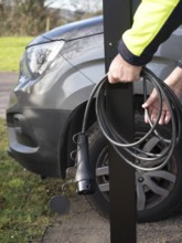 Worker holding ev charging cable next to vehicle, preparing for installation