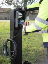 Worker installing an ev charging point, connecting wires and using a power tool for sustainable