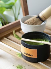 Green tea matcha powder spilling from a measuring scoop on a wooden tray