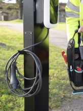 Electrician installing a new outdoor electric vehicle charging station with cable