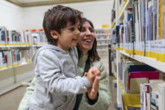 Happy mother and son enjoying a moment of discovery and learning while looking for books on shelves
