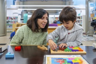 Woman and boy are playing with a colorful wooden tangram puzzle, focusing on solving the geometric