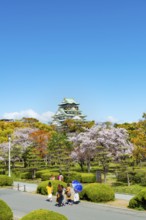 Osaka castle with blooming cherry trees in the park, visitors on a path through Osaka Castle Park,