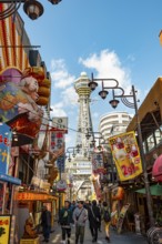 Lots of colorful signs in a pedestrian zone with shops and restaurants, behind Tsutenkaku Tower,