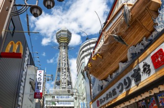 Lots of colorful signs in a pedestrian zone with shops and restaurants, behind Tsutenkaku Tower,