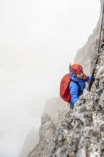 Mountaineers on a ladder on the Via Ferrata Oliva Detassis via ferrata in fog, rocky mountain peaks