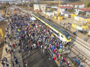 Many people at an event with train and construction site near a train station, opening of the