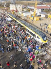 Many people gather at an event near a construction site by train at a train station, opening of the
