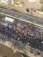 People gather around a parked train at a train station, aerial view, opening of the Hermann Hesse