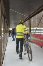 Cyclist wearing yellow safety clothing pushes a bicycle across a modern bridge, opening of the