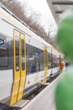 A yellow and white train stands on the platform with people and green balloons, opening of the