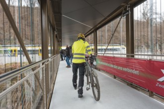 Person wearing yellow safety vest pushes bicycle across a covered bridge, opening of the Hermann