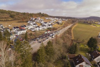 Aerial view of a rural village with a crowd of people on a railroad track, surrounded by hills and