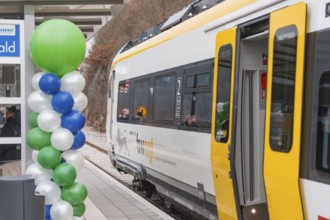 A yellow and white train at the train station with colorful balloons in the foreground, opening of