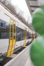 Yellow and white train on a platform with colorful balloons in the foreground, opening of the
