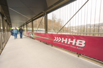 Pedestrian bridge with a large Hermann Hesse Railway banner and people crossing the bridge, opening