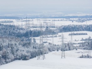 Snow-covered fields with electricity poles and a village in the background under a blue sky,
