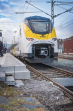 A modern SWEG train stops at the station. Blue-yellow accents contrast with the blue sky, battery