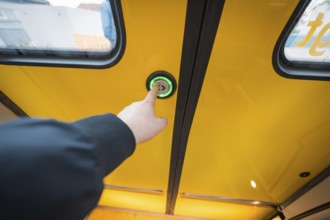 Hand presses button on yellow train door, surrounded by windows, battery electric train Siemens