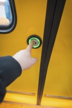 Close-up of a hand pressing a green door button on a yellow train, battery electric train Siemens